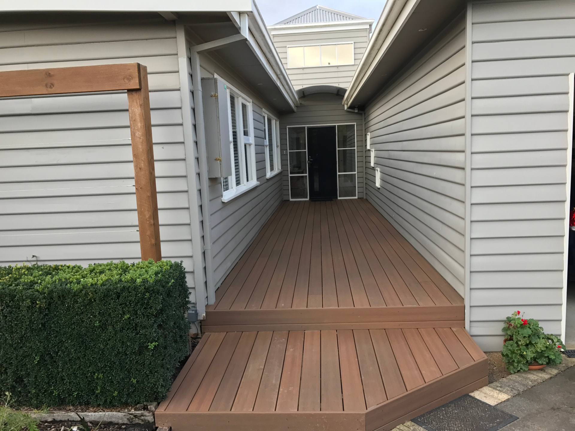Brown composite entry deck with wide stair treads leading to a front door between white weatherboard walls