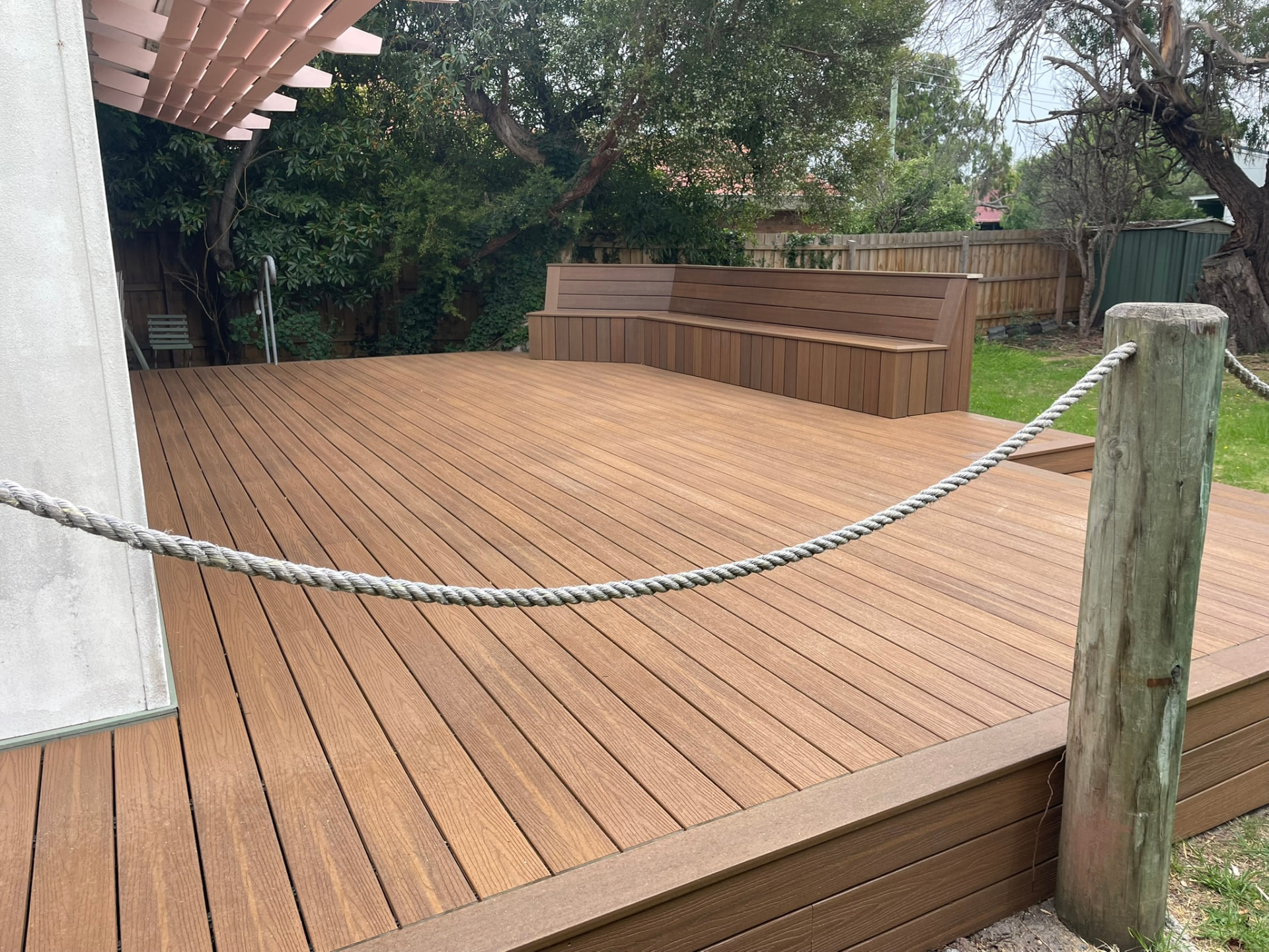Composite deck with built-in corner bench seating and rope balustrade in a backyard