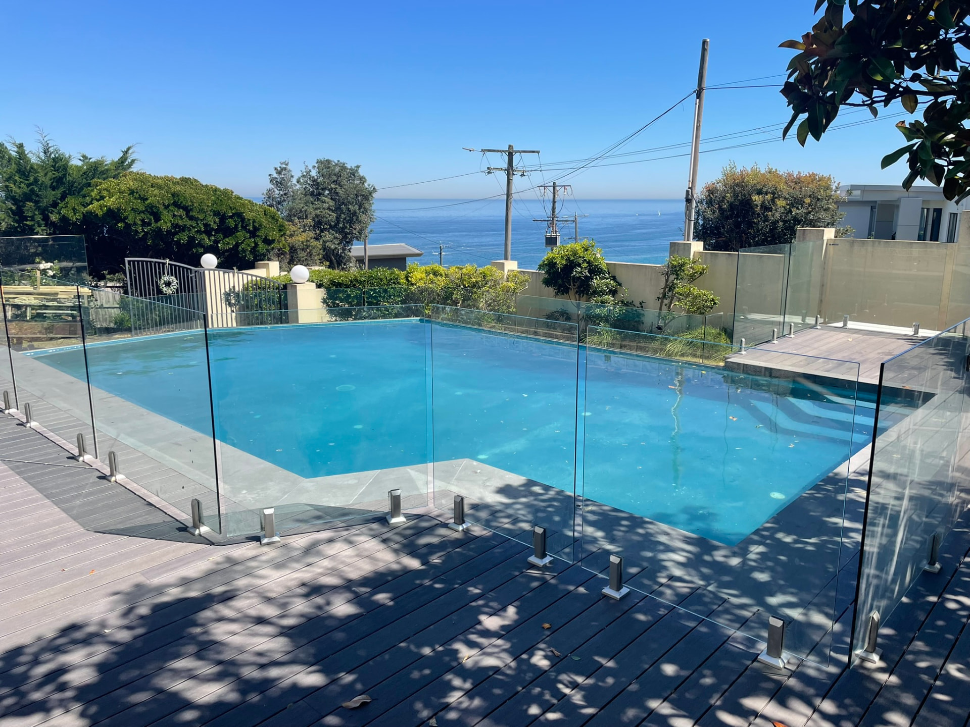 Grey composite pool surround deck with frameless glass fencing overlooking the ocean