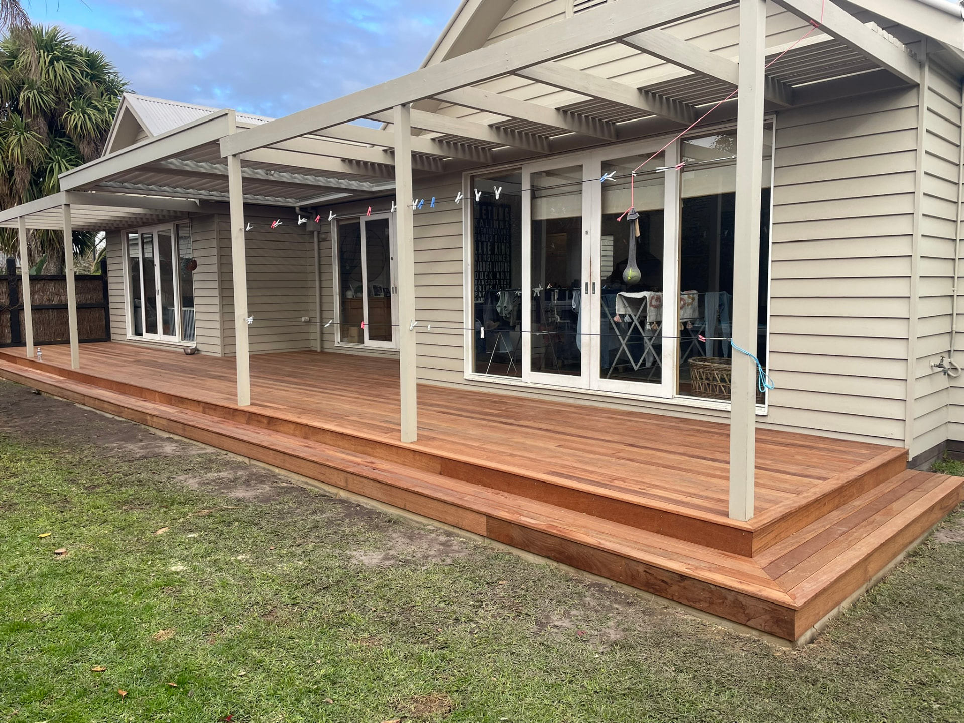 Timber backyard deck with stepped edges and white pergola posts beside a lawn